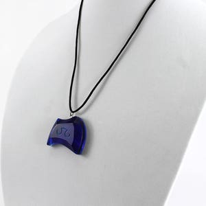 May include: A blue glass pendant necklace with a curved shape and a white design. The necklace is on a black cord.
