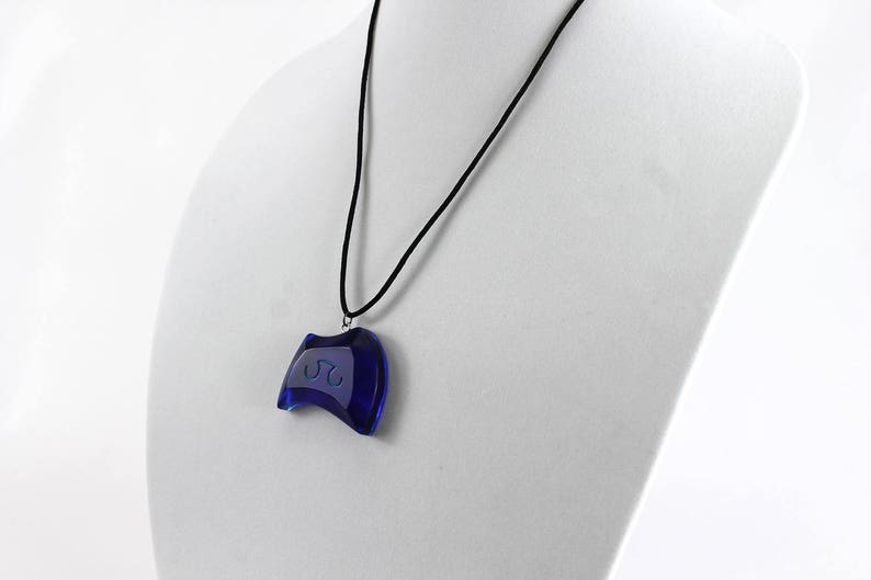 May include: A blue glass pendant necklace with a curved shape and a white design. The necklace is on a black cord.