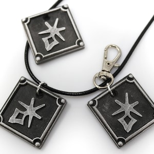 May include: A black necklace with three silver square pendants featuring a stylized kanji character. The necklace has a silver lobster clasp.