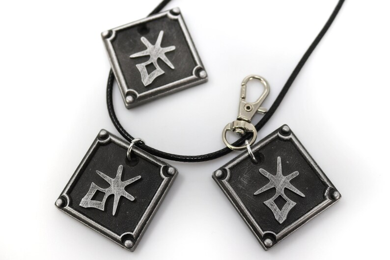 May include: A black necklace with three silver square pendants featuring a stylized kanji character. The necklace has a silver lobster clasp.