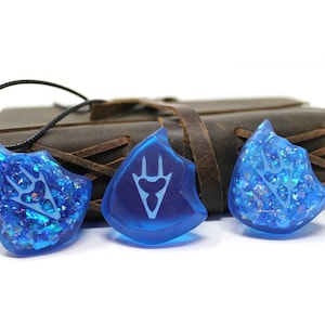 May include: Three blue resin pendants with a white design. The pendants are shaped like a shield and have a sparkly finish.