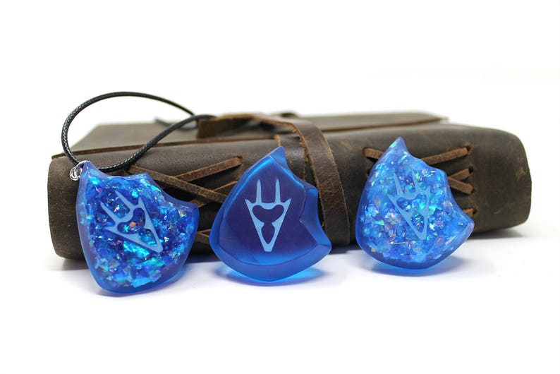 May include: Three blue resin pendants with a white design. The pendants are shaped like a shield and have a sparkly finish.
