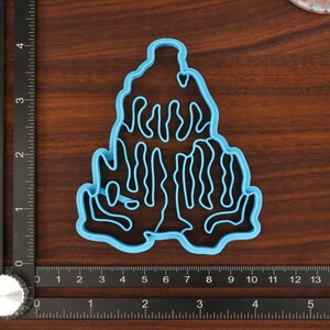 Puede incluir: Un cortador de galletas de pl&aacute;stico azul con forma de &aacute;rbol estilizado con un dise&ntilde;o ondulado y org&aacute;nico. El cortador est&aacute; sobre una superficie de madera.