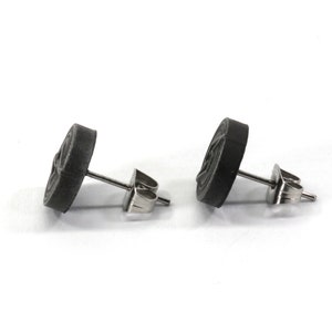 May include: A pair of black stud earrings with a circular design. The earrings have a silver post and butterfly backing.