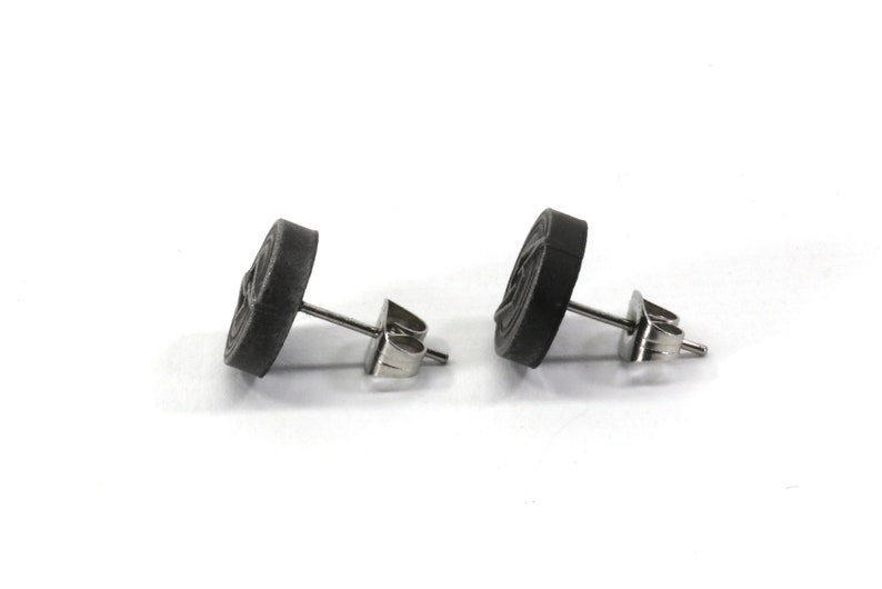 May include: A pair of black stud earrings with a circular design. The earrings have a silver post and butterfly backing.