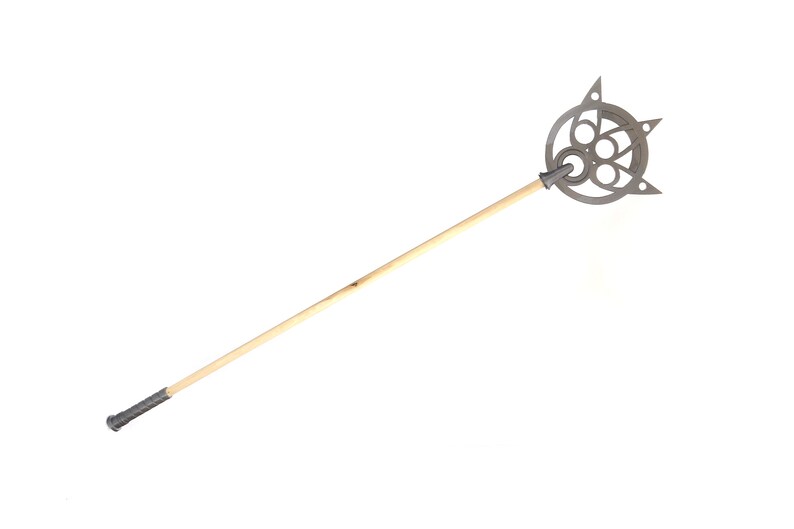 May include: A wooden staff with a silver metal head featuring a circular design with multiple holes. The head has a pointed tip and a decorative design.