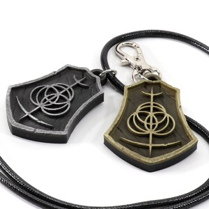 May include: Two silver and gold pendants with a black cord. The pendants feature a circular design with a cross in the center.