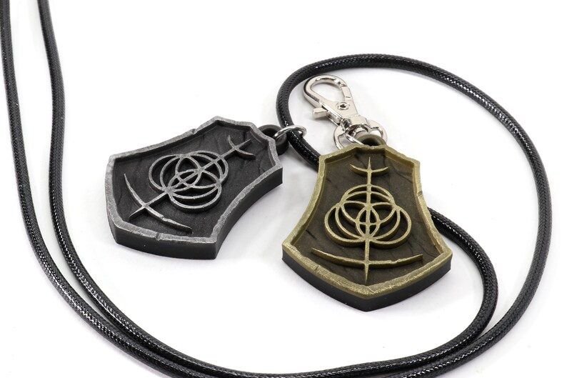 May include: Two silver and gold pendants with a black cord. The pendants feature a circular design with a cross in the center.