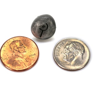 May include: A silver metal bead with a rune symbol engraved on it. The bead is about the size of a dime.