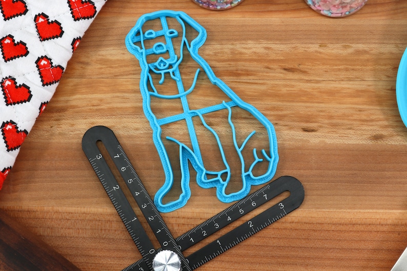 Peut inclure: Un emporte-pi&egrave;ce en plastique bleu en forme de chien assis. L'emporte-pi&egrave;ce est sur une surface en bois avec une r&egrave;gle.