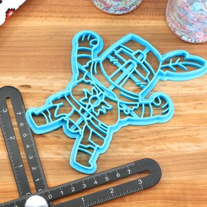 May include: A blue plastic cookie cutter shaped like a cartoon knight holding a sword and shield. The knight is wearing a helmet and armor.