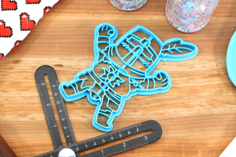 May include: A blue plastic cookie cutter shaped like a cartoon knight holding a sword and shield. The knight is wearing a helmet and armor.