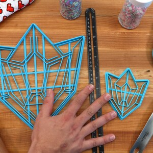 Puede incluir: Dos cortadores de galletas de pl&aacute;stico azul con forma de cristales geom&eacute;tricos. El cortador m&aacute;s grande mide aproximadamente 15 cm de ancho y el m&aacute;s peque&ntilde;o aproximadamente 7,5 cm de ancho.