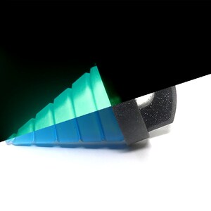 May include: A close-up of a multi-colored, geometric object. The object is primarily blue and green, with a black section on the right. The object appears to be made of a translucent material, with a stepped design.