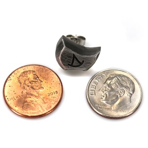 May include: A silver earring with a geometric design and a post back. The earring is shown next to a US penny and a dime for size comparison.