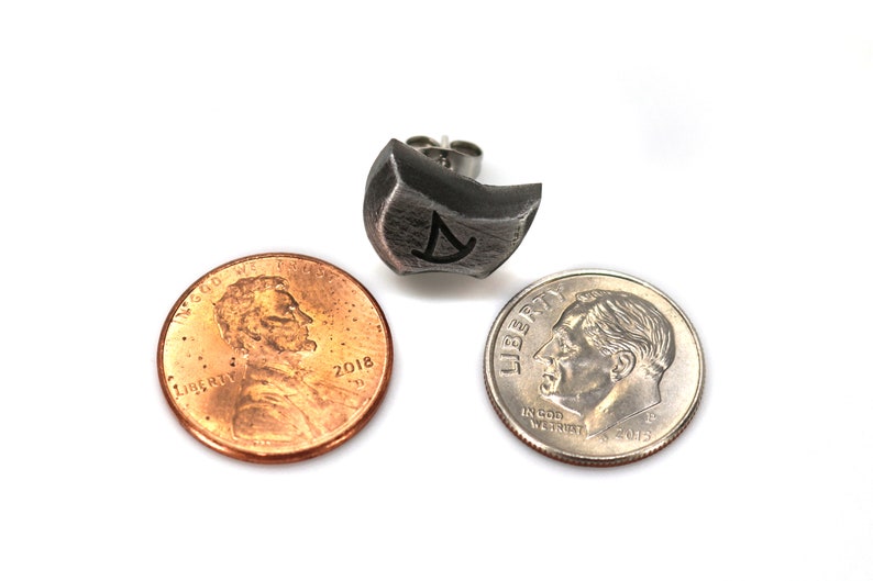 May include: A silver earring with a geometric design and a post back. The earring is shown next to a US penny and a dime for size comparison.