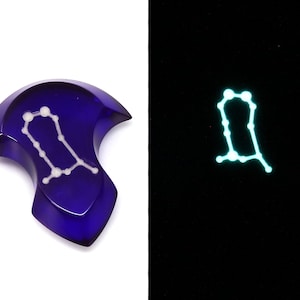 May include: A dark blue, crescent-shaped, glass paperweight with a white outline of the Gemini constellation. The paperweight glows green in the dark.