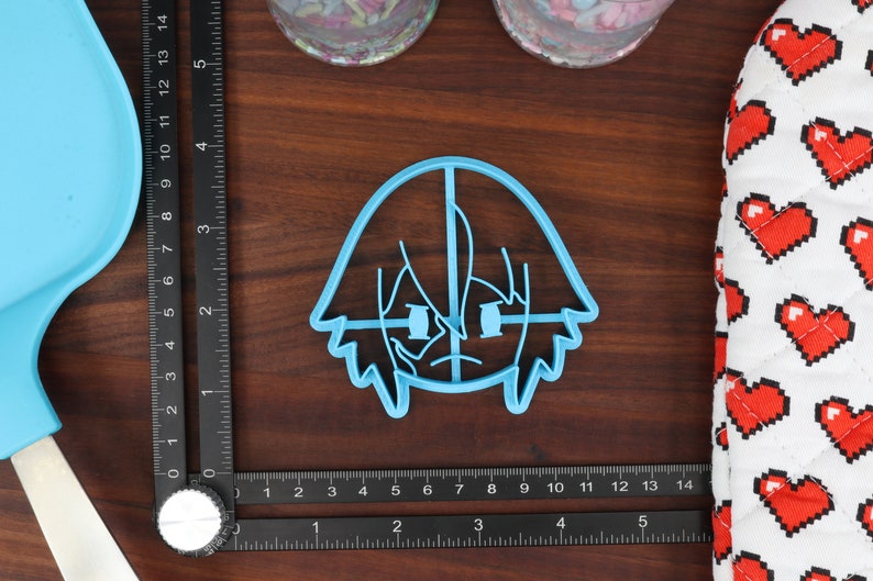 May include: A light blue plastic cookie cutter shaped like a cartoon character with short, spiky hair and a serious expression.