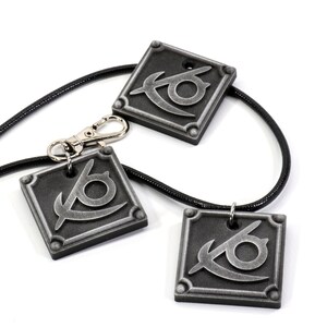 May include: Three silver-colored pendants with a stylized eye design, hanging on black cords. Two of the pendants are attached to the cords, while the third pendant is attached to a silver-colored clasp.