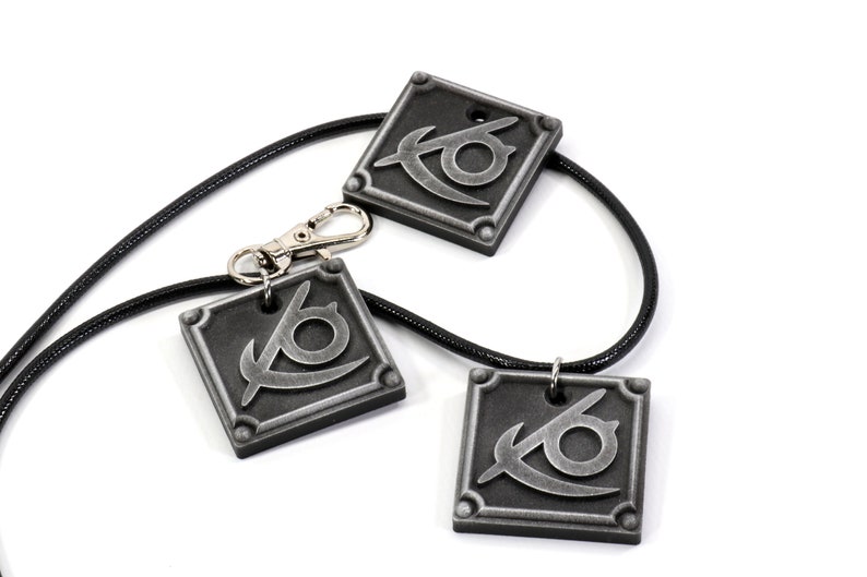May include: Three silver-colored pendants with a stylized eye design, hanging on black cords. Two of the pendants are attached to the cords, while the third pendant is attached to a silver-colored clasp.