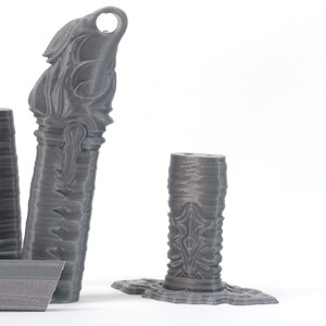 May include: Three gray 3D printed decorative pieces with intricate designs. The pieces are tall and slender, with a cylindrical shape. The designs are abstract and geometric, with a textured surface.