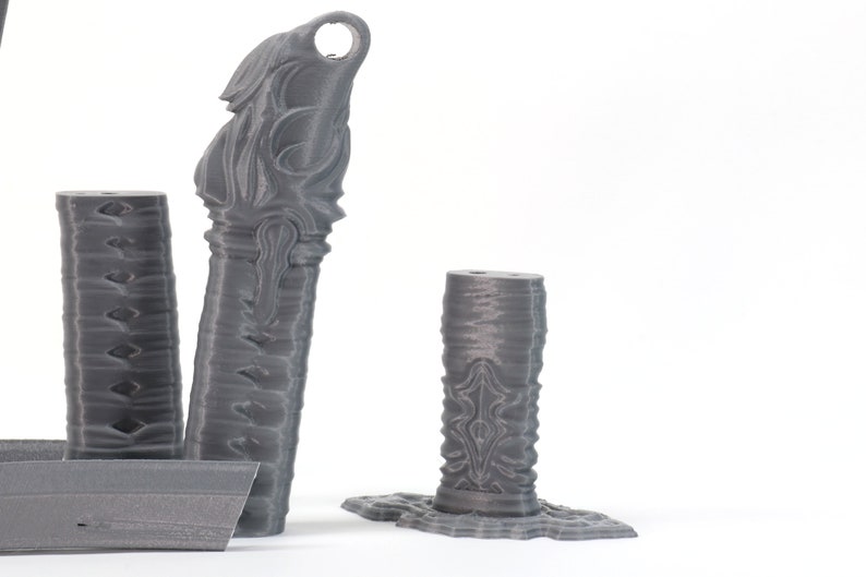 May include: Three gray 3D printed decorative pieces with intricate designs. The pieces are tall and slender, with a cylindrical shape. The designs are abstract and geometric, with a textured surface.