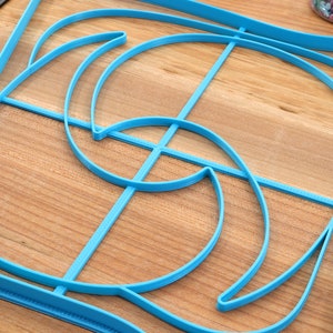 May include: A blue plastic template with a complex geometric design. The template is made up of multiple curved lines and shapes.