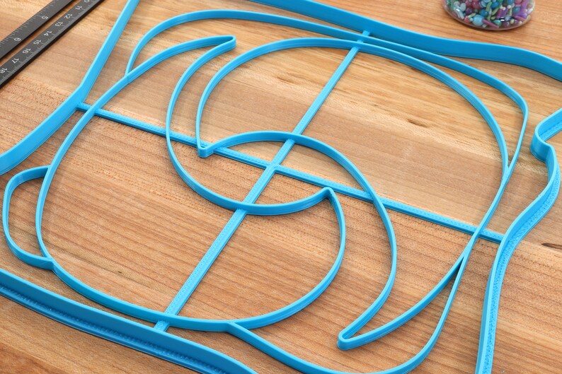 May include: A blue plastic template with a complex geometric design. The template is made up of multiple curved lines and shapes.