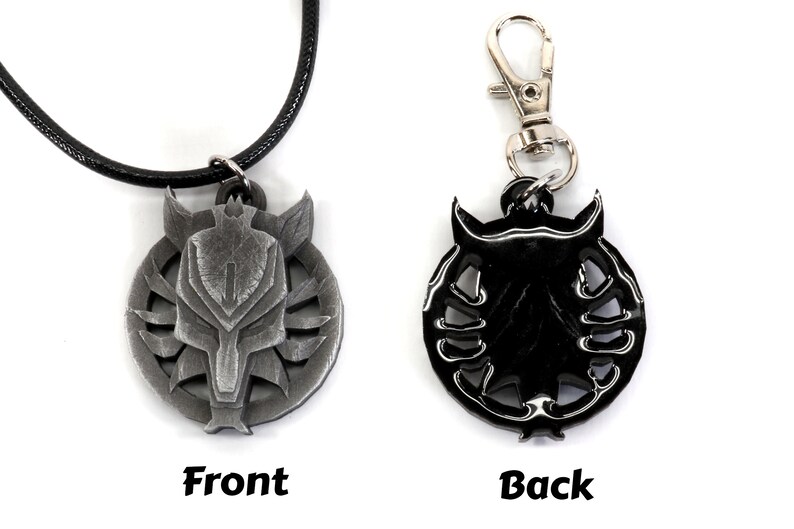 Op de afbeelding: Een zilverkleurige ketting met een wolfskopontwerp aan de voorkant en een zwart, gedetailleerd ontwerp aan de achterkant. De ketting heeft een zwart koord.