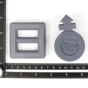May include: Two gray plastic objects. One is a square with a rectangular opening and a smaller rectangular opening inside. The other is a round object with an arrow pointing up and the text "AO2" inside.