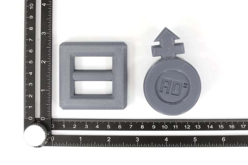 May include: Two gray plastic objects. One is a square with a rectangular opening and a smaller rectangular opening inside. The other is a round object with an arrow pointing up and the text "AO2" inside.