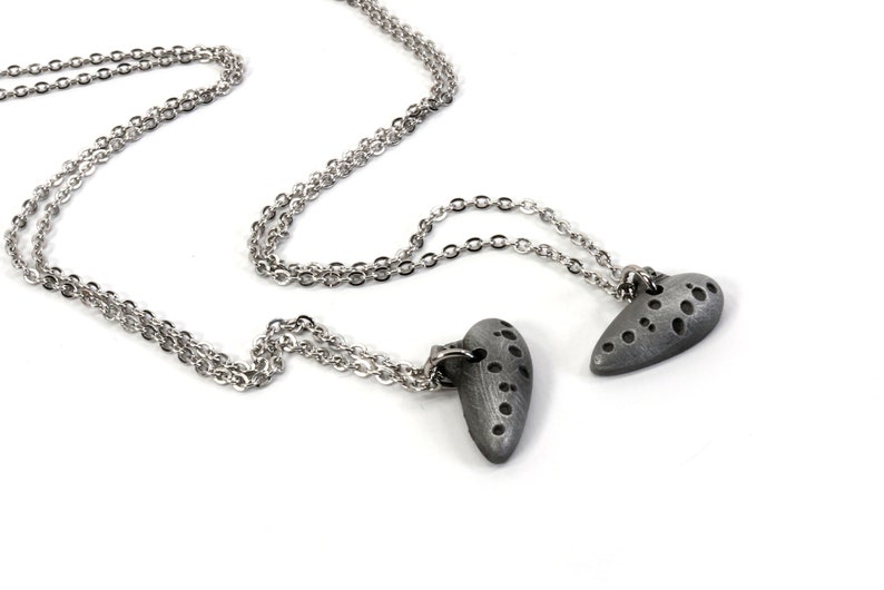 May include: Two silver chains with heart-shaped pendants. The pendants are textured and have a gray finish.
