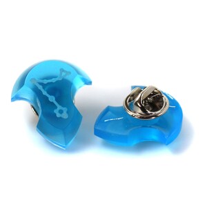 May include: A blue enamel pin with a silver pin back. The pin features a white outline of the constellation Aquarius.