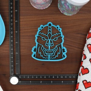 May include: A blue plastic cookie cutter shaped like a monster with a toothy grin and a single horn on its head.