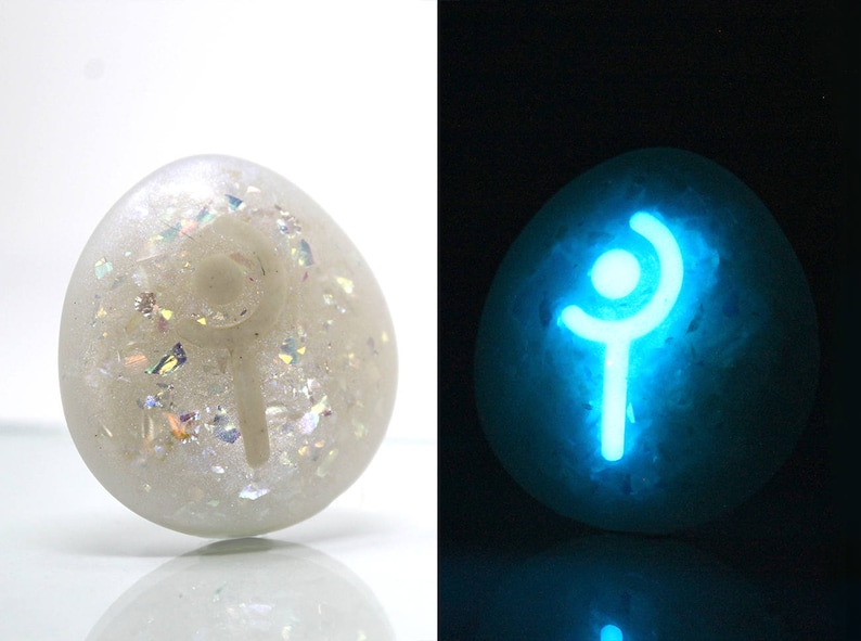 K&ouml;nnte beinhalten: Ein wei&szlig;er Stein mit einem leuchtend blauen Symbol darauf. Das Symbol ist eine stilisierte Strichm&auml;nnchenfigur mit einer geschwungenen Linie &uuml;ber dem Kopf. Der Stein ist eine beliebte Wahl f&uuml;r Fans von Fantasy- und Rollenspielen.