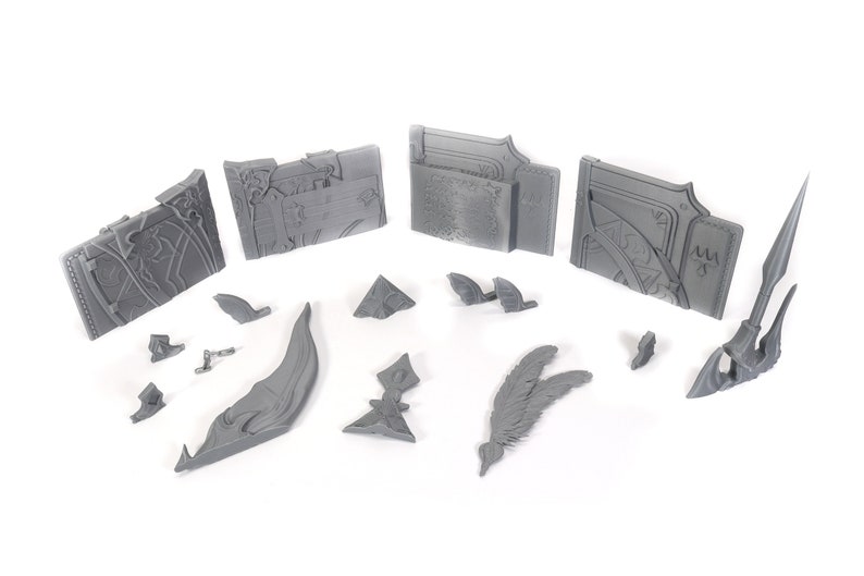 May include: A set of 3D printed gray plastic pieces for a model kit. The pieces include a spear, a wing, a curved piece, and several rectangular pieces with intricate designs.