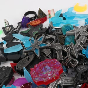 May include: A collection of colorful and metallic charms, including stars, swords, and other abstract shapes. The charms are made of various materials, including metal, plastic, and resin.