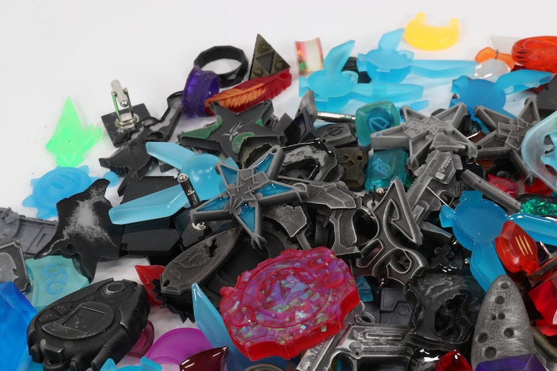 May include: A collection of colorful and metallic charms, including stars, swords, and other abstract shapes. The charms are made of various materials, including metal, plastic, and resin.