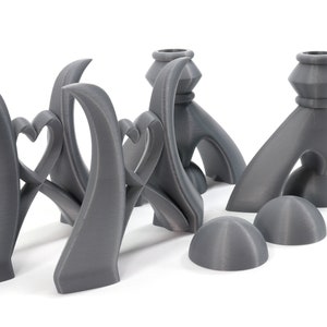 May include: Set of five gray 3D printed candle holders. The candle holders are shaped like hearts and have a modern design.