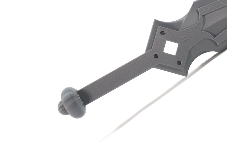 May include: A gray plastic sword with a rounded handle and a detailed hilt. The hilt has a square opening and several small holes.