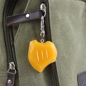 May include: A yellow charm with three lines on a silver chain attached to a green canvas bag.