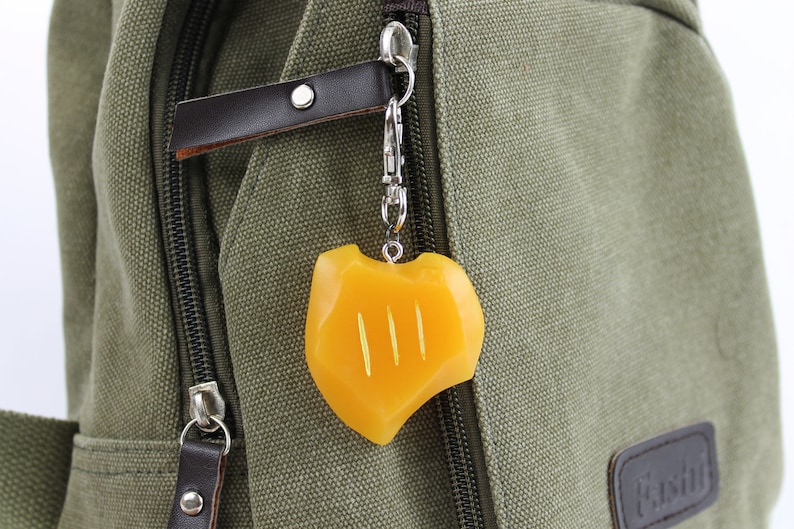 May include: A yellow charm with three lines on a silver chain attached to a green canvas bag.