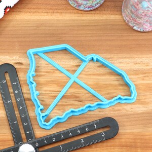 May include: A blue plastic cookie cutter shaped like the state of South Carolina. The cutter is on a wooden surface with a ruler and other baking supplies.