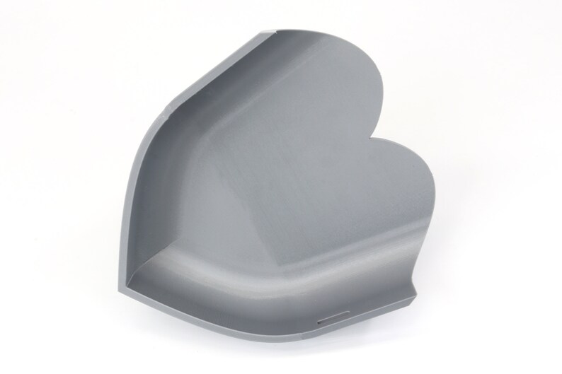 May include: A gray, heart-shaped corner shelf, likely for decorative or storage purposes. The shelf has a smooth, matte finish and a curved design. The product is made of a solid material and is set against a white background.