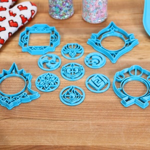 May include: A set of blue plastic cookie cutters featuring various geometric and abstract designs. The cutters are arranged on a wooden surface.