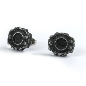 May include: A pair of silver earrings with a detailed design resembling a futuristic watch face.
