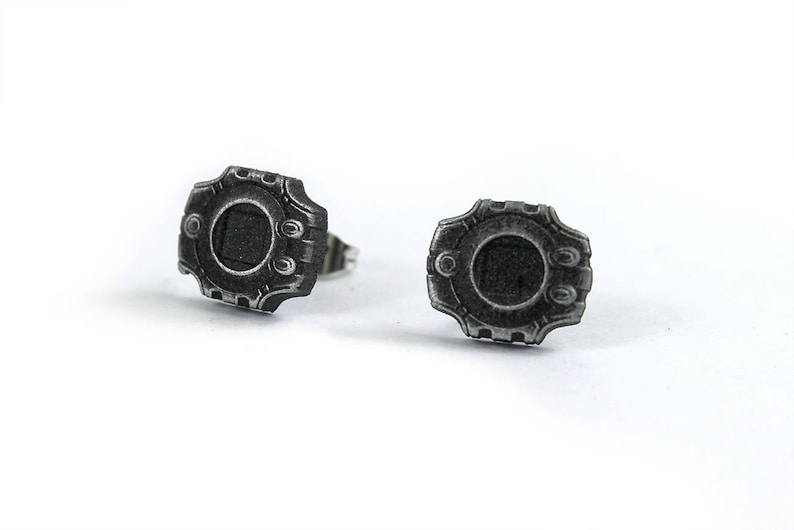 May include: A pair of silver earrings with a detailed design resembling a futuristic watch face.
