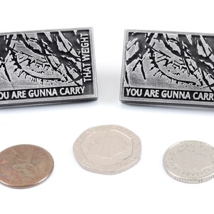 May include: Two silver pins with a black and white graphic of a tree branch and the text "You are gunna carry that weight". Three coins are also shown in the image.