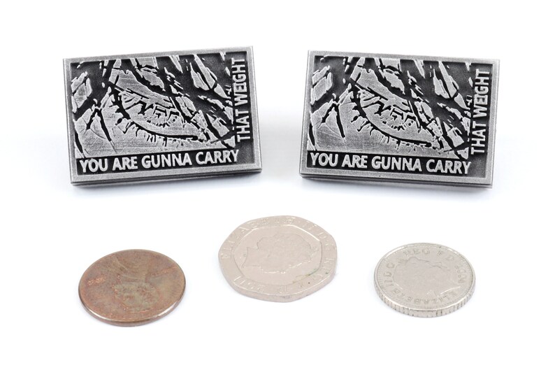 May include: Two silver pins with a black and white graphic of a tree branch and the text "You are gunna carry that weight". Three coins are also shown in the image.