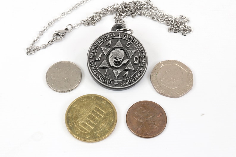 May include: A silver-colored pendant necklace with a circular pendant featuring an engraved design and text. The pendant is on a silver chain. Several coins of different sizes and colors are arranged around the pendant.